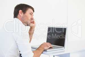 Thinking businessman sitting at desk using laptop