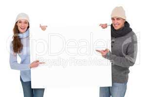Casual couple in warm clothing holding poster