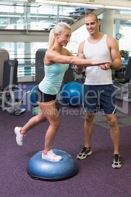 Trainer assisting woman with stretching exercises at gym
