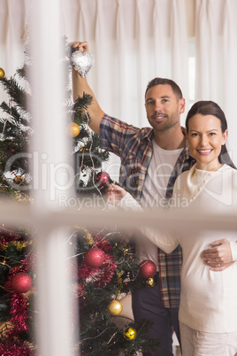 Smiling couple decorating the christmas tree together