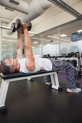 Fit man lifting dumbbell lying on the bench