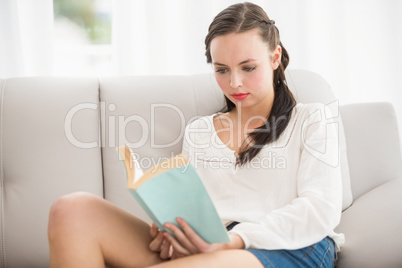 Pretty brunette reading book on couch