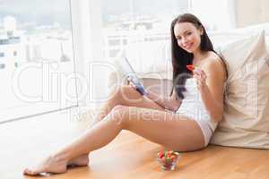 Pretty brunette using tablet pc sitting on floor