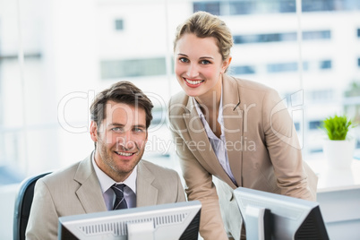 Smiling businessman helping his colleague at a computer