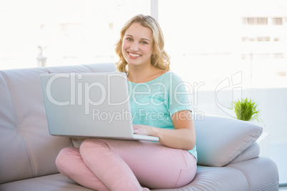 Happy casual blonde relaxing on couch using laptop