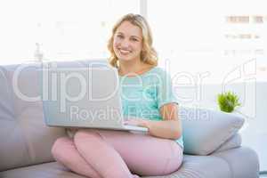 Happy casual blonde relaxing on couch using laptop