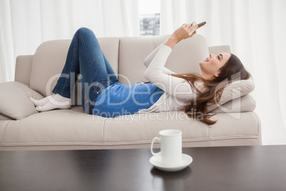 Pretty brunette sending a text on the couch