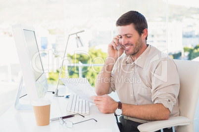 Smiling businessman making a call and reading a document