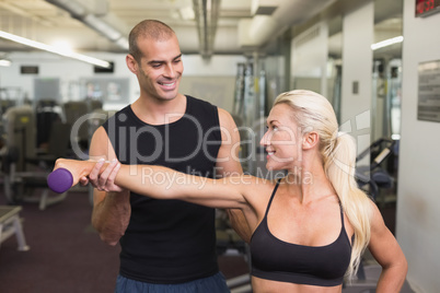 Male trainer assisting woman with dumbbell in gym