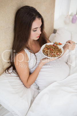 Pregnant brunette eating cereal in bed