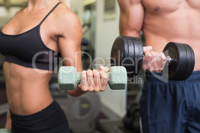 Mid section of couple exercising with dumbbells in gym