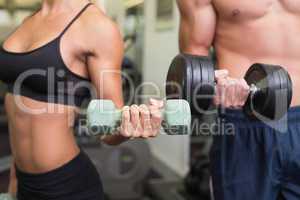 Mid section of couple exercising with dumbbells in gym