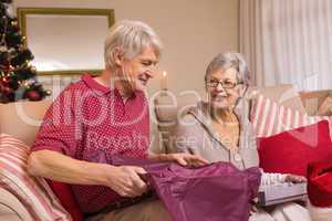 Senior couple opening a christmas present on sofa