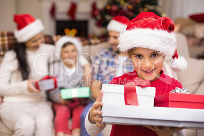 Festive daughter holding pile of gifts with his family behind