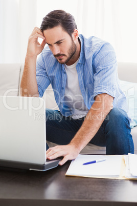 Worried man sitting at table using laptop to pay his bills