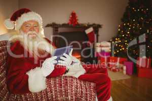 Cheerful santa using tablet on the couch