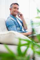 Happy man sitting on couch phoning and using laptop