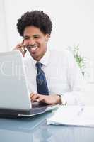 Smiling businessman on the phone and using laptop