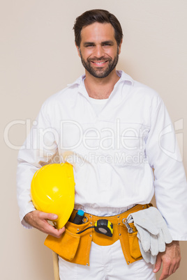 Handyman holding his yellow helmet in tool belt