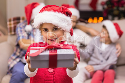 Smiling little girl offering a gift with her parents behind