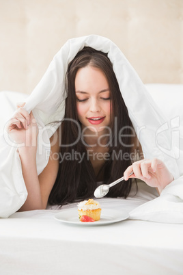 Pretty brunette eating cupcake in bed