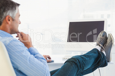 Relaxed man with feet on desk using computer
