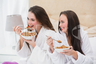 Pretty friends wearing bathrobes eating cereal