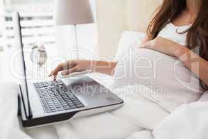 Pregnant brunette using laptop in bed