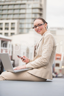 Young businesswoman using laptop holding her phone