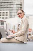 Young businesswoman using laptop holding her phone