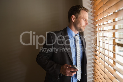 Man peeking through blinds while holding his phone