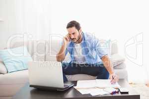 Man paying his bills with laptop while talking on phone