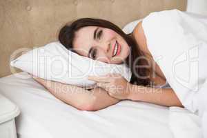 Pretty brunette lying in bed smiling at camera