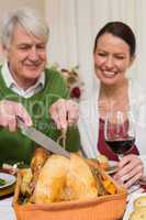 Grandfather carving chicken while woman drinking red wine