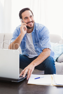 Man paying his bills with laptop while talking on phone