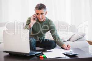 Man with laptop phoning and taking notes