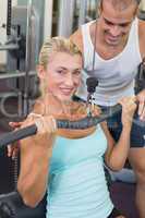 Male trainer assisting beautiful young woman on lat machine
