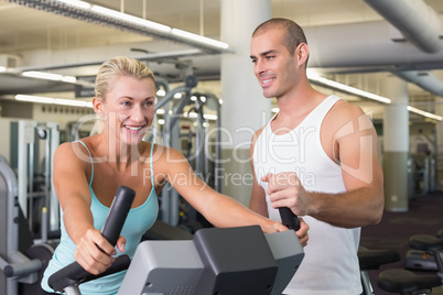 Trainer assisting woman with exercise bike at gym