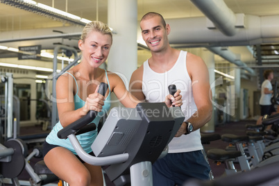 Male trainer assisting woman with exercise bike at gym