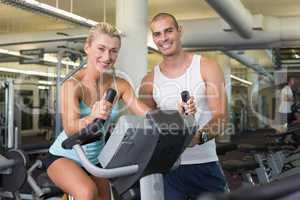 Male trainer assisting woman with exercise bike at gym