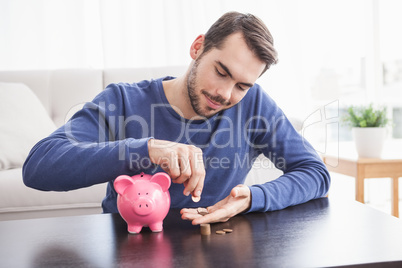 Young man putting coins in piggy bank
