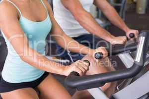 Mid section of couple working on exercise bikes at gym