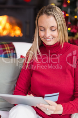 Festive blonde woman using her credit card and tablet pc