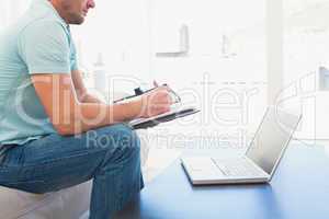 A man writing on a notebook sitting on a sofa