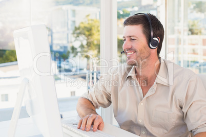 Smiling casual businessman listening to computer at desk