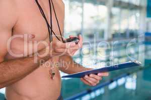Mid section of shirtless coach with stopwatch by pool at leisure