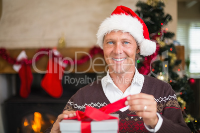 Smiling handsome man in santa hat opening a gift