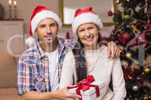 Smiling couple in santa hat holding present