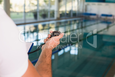 Cropped swimming coach with stopwatch by pool at leisure center