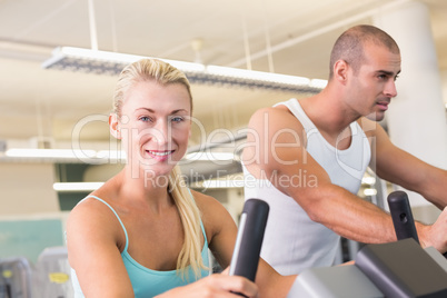 Fit young couple working on exercise bikes at gym